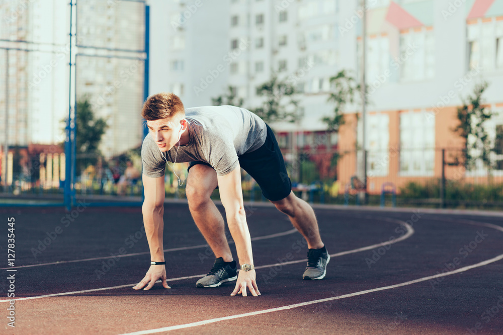 Young handsome guy in the morning on stadium. He wears sport clothes, listening to music through headphones, going to run. Young handsome guy in the morning on stadium. He wears sport clothes, listening to music through headphones, going to run.