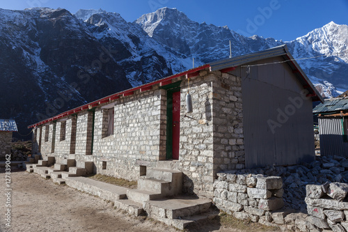 Remote school in Himalayan village of Thame, Sagarmatha National Park, Nepal. Nepali house made of stones with wall of snowy mountains behind it. photo