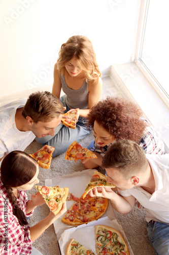 Friends having fun and eating pizza while sitting on floor