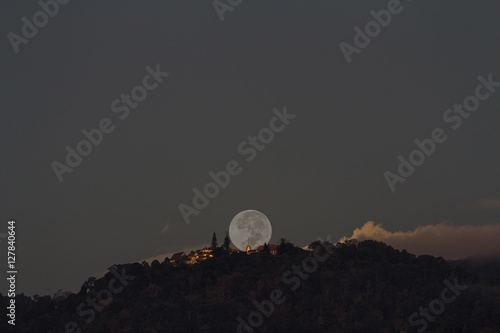 Supermoon setting over Buddhist temple on mountain at early morning  focus at temple