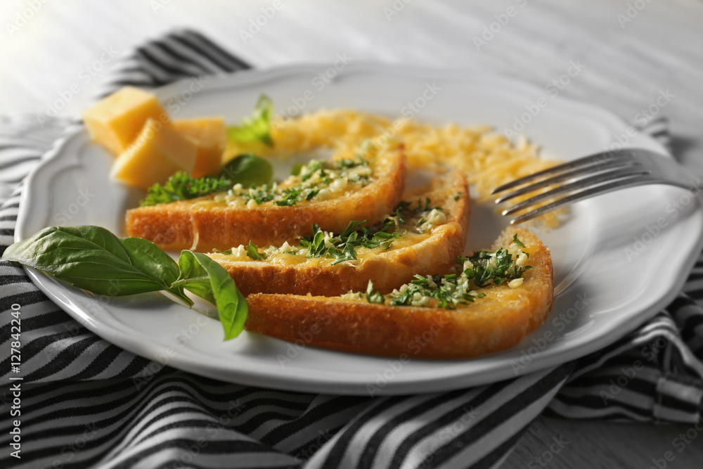 Plate with tasty garlic French bread slices and striped napkin