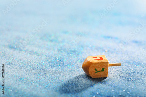 Wooden dreidel for Hanukkah on light sparkling background