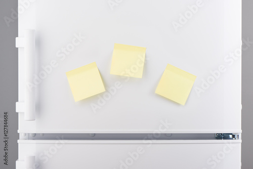 Blank light yellow sticky paper notes on white refrigerator