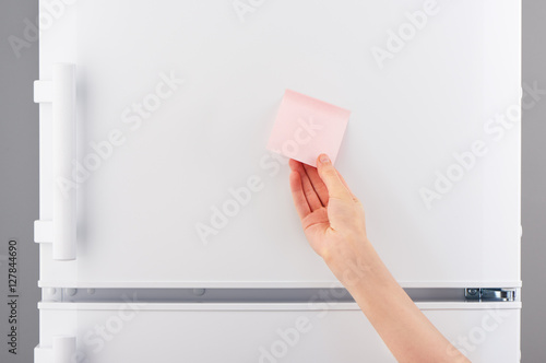 Female hand holding pink paper note on white refrigerator