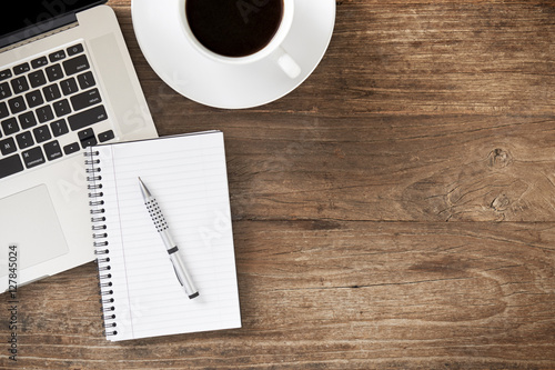 Laptop computer with notepad, pen and coffee on wooden table
