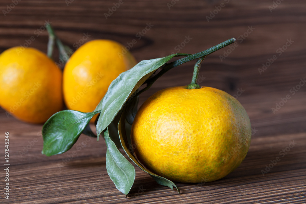 Ripe tangerines (mandarins) with leaves on dark wooden background