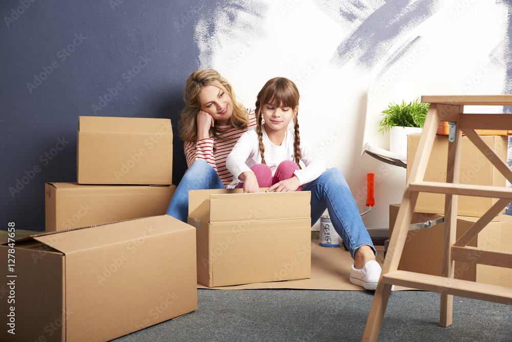 Moving into a new home. Shot of a cute girl helping to unpack the cardboard box to her mother while sitting their new home. Moving into a new home. Shot of a cute girl helping to unpack the cardboard box to her mother while sitting their new home.