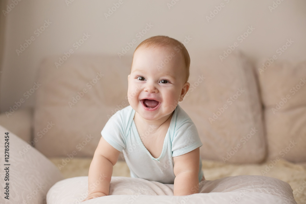 Cute smiling baby in blue bodysuit on a beige couch.