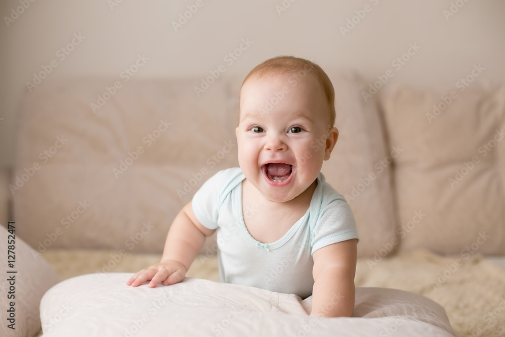 Cute smiling baby in blue bodysuit on a beige couch.