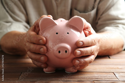 Vászonkép Hands of old senior with piggybank on a wooden table