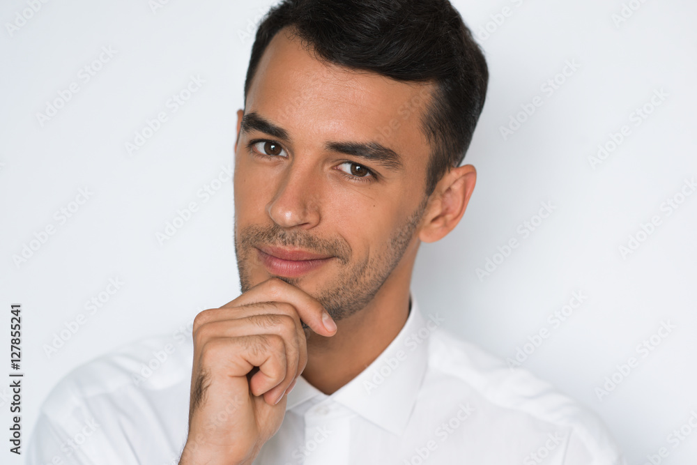 Portrait of attractive young man smiling with hand on chin. Isolated on light gray background. Beautiful businessman thinking. Portrait of attractive young man smiling with hand on chin. Isolated on light gray background. Beautiful businessman thinking.
