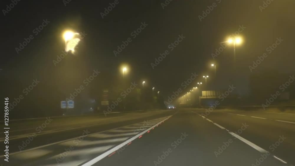 Car driver's point of view driving on a foggy motorway in England with streetlights at night Car driver's point of view driving on a foggy motorway in England with streetlights at night