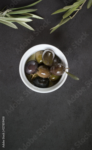 Black olives in dark background with olive tree leaves. Vertical image with copy space for you text.