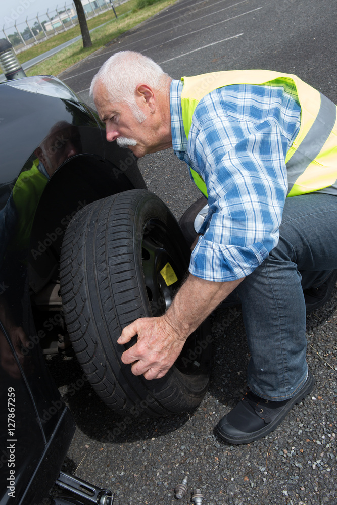 aged man changing leaking tire on the verge
