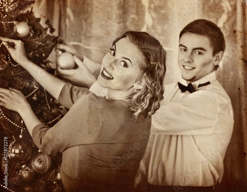Couple on party decoration Christmas tree. Black and white retro.Old photo on yellow paper.