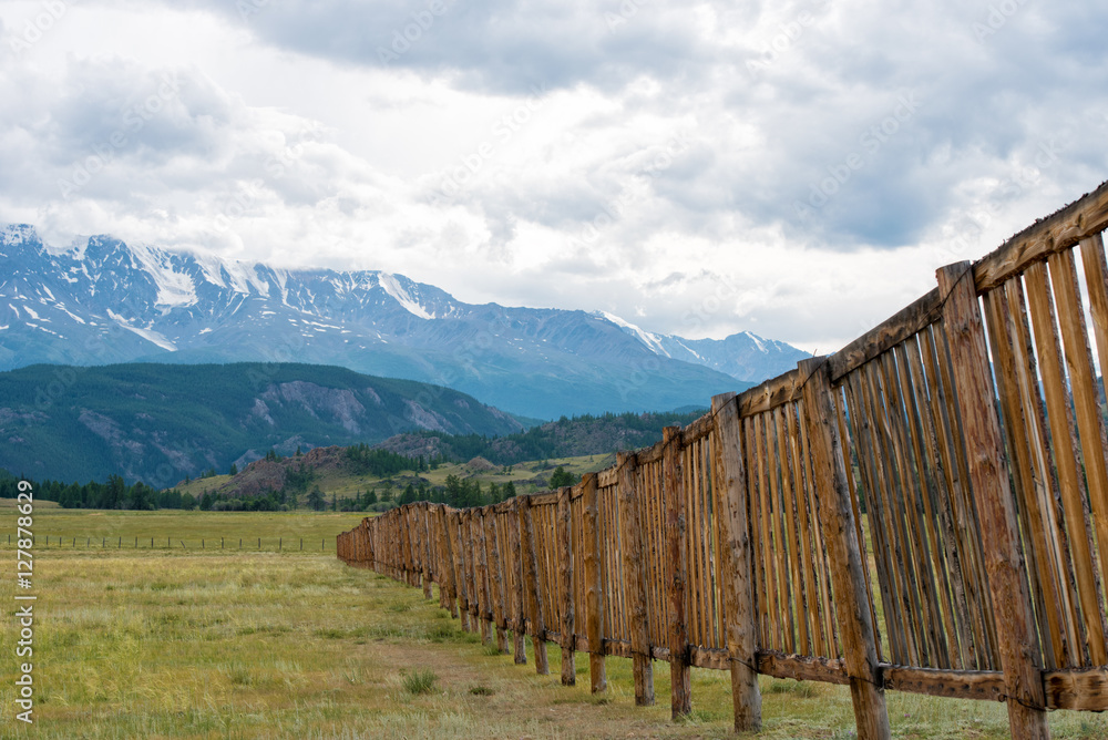 Fototapeta premium Long wooden fence in a field. In the distance the mountains.