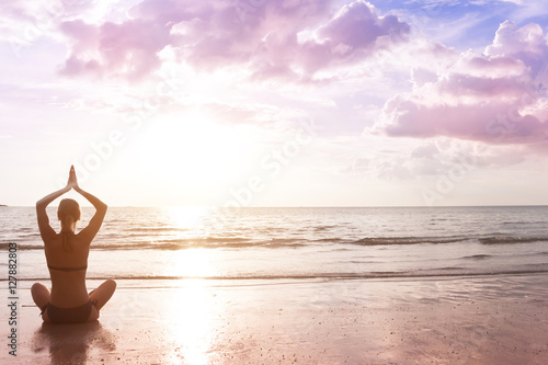 Young woman makes meditation in lotus pose on sunset sea beach, harmony and contemplation.