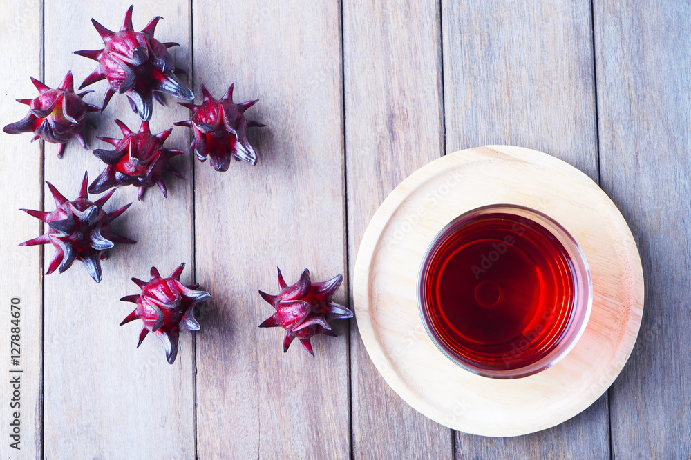 Top view of a glass of roselle juice and fresh roselle on a wooden table. Top view of a glass of roselle juice and fresh roselle on a wooden table.