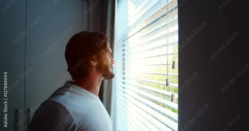 Man looking through window blinds after waking up Man looking through window blinds after waking up