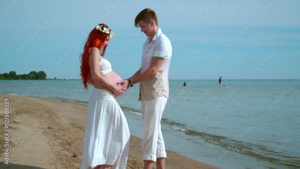 Pregnant couple beach. Man holding pregnant belly in hands. Expecting