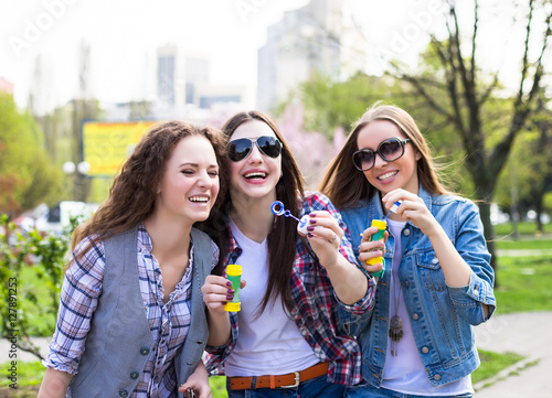 Teen girls blowing soap bubbles. Young happy teenagers having fun in summer park.