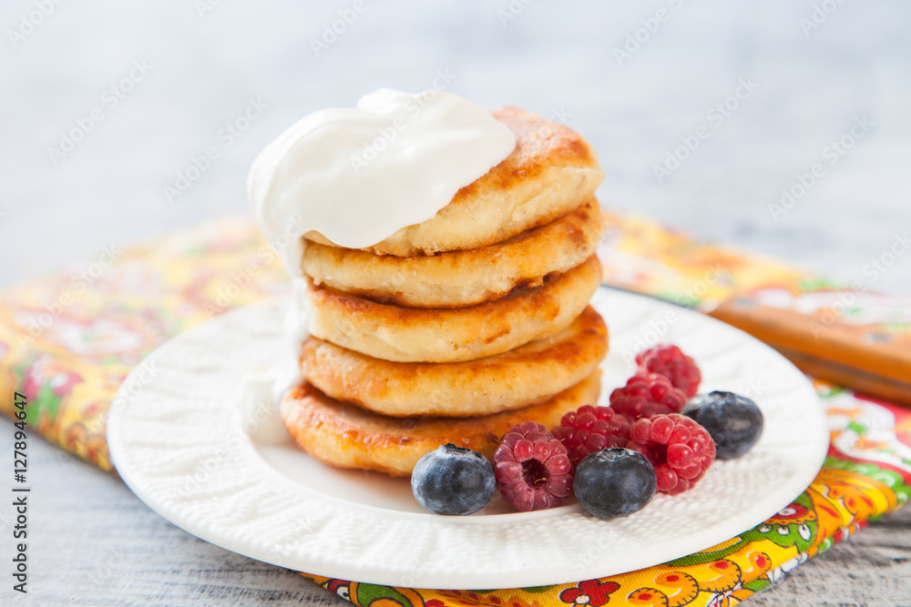 Summer cottage cheese pancakes on white plates on a  table with sour cream and berry, closeup, selective focus