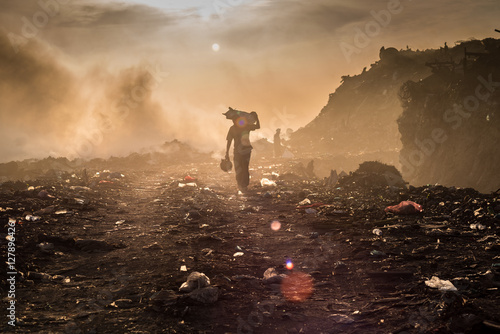 A waste picker is collecting reusable or recyclable materials in a open burning dump. photo