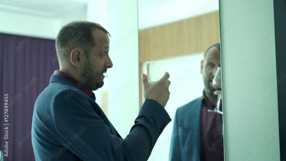 Drunk businessman drinking wine and talking to mirror at home
Drunk businessman drinking wine and talking to mirror at home