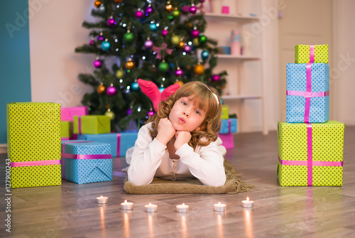 Girl lying on the floor next to the presents and a tree