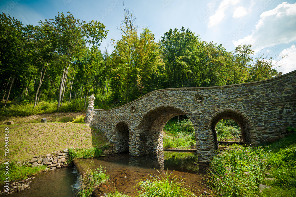 A stone bridge over a river in summer at the park.