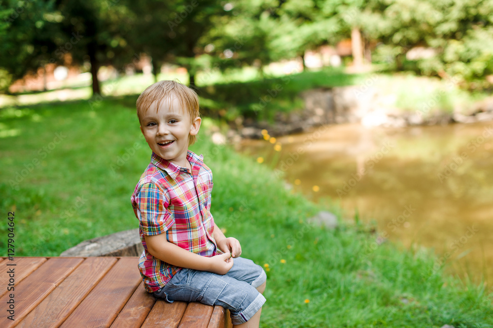 Smiling happy boy sitting on bench near lake. Summer time weeken Smiling happy boy sitting on bench near lake. Summer time weeken