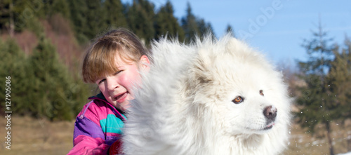 Little girl playing with samoyed on the snow