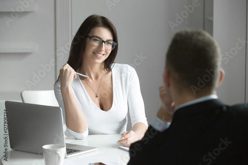 Canvas Print Young smiling beautiful businesswoman talking to a male job applicant at the desk, interviewing flirting with a coworker