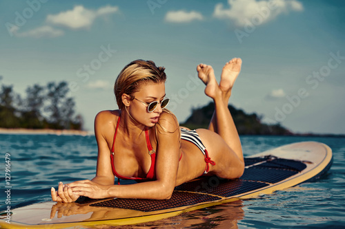 Sexy woman lying on a surfing board on the water in the sea
