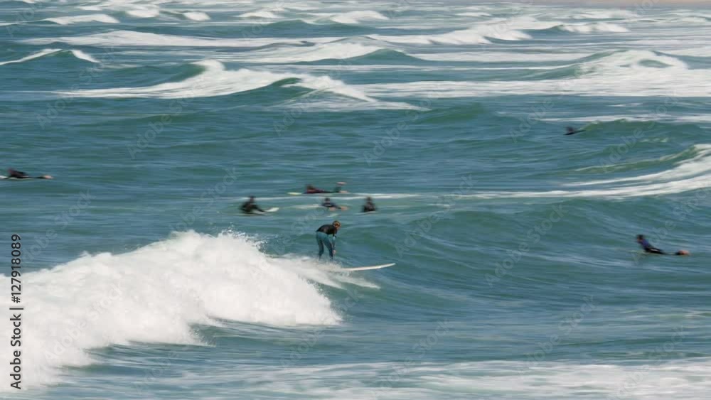 A young, inexperienced surfer manages to ride a wave, surrounded by surfers wading in the ocean, waiting for that big wave. A young, inexperienced surfer manages to ride a wave, surrounded by surfers wading in the ocean, waiting for that big wave.