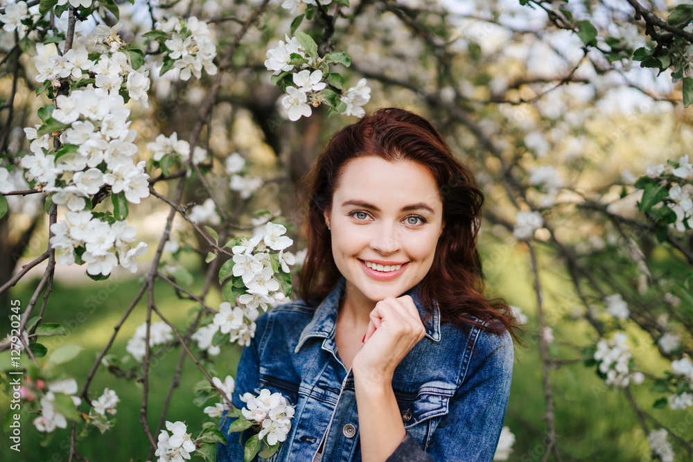 Young pretty smiling caucasian woman in jeans jacket standing near blooming spring tree. Youth, freshness, beauty, happiness concept. Young pretty smiling caucasian woman in jeans jacket standing near blooming spring tree. Youth, freshness, beauty, happiness concept.