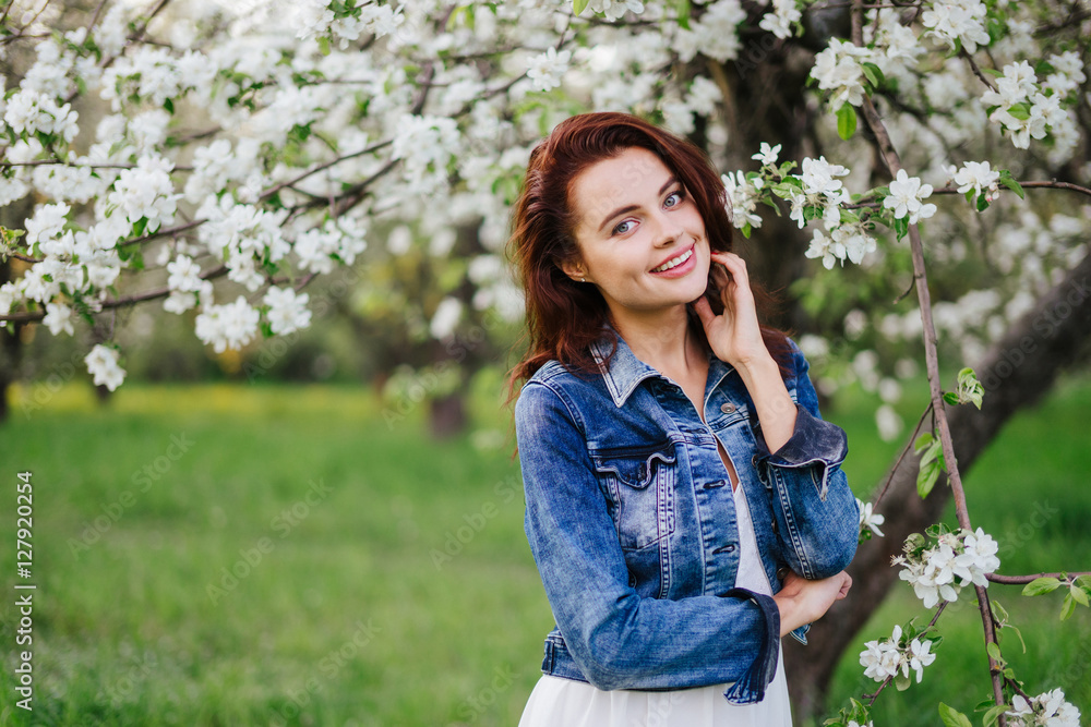 Young pretty smiling caucasian woman in jeans jacket standing near blooming spring tree. Youth, freshness, beauty, happiness concept. Young pretty smiling caucasian woman in jeans jacket standing near blooming spring tree. Youth, freshness, beauty, happiness concept.