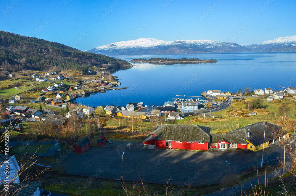 Scandinavian landscape with alone houses and beautiful blue lake and snowy mountains in background