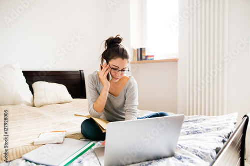 Woman sitting on bed, working on laptop, calling. Home office.