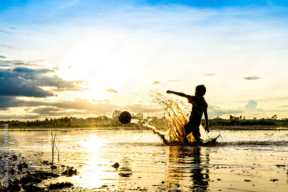 Silhouette of boy playing football in water
