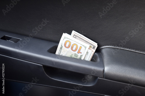 Several notes of US dollars and are folded in half in the door handle of the car. The money in the car