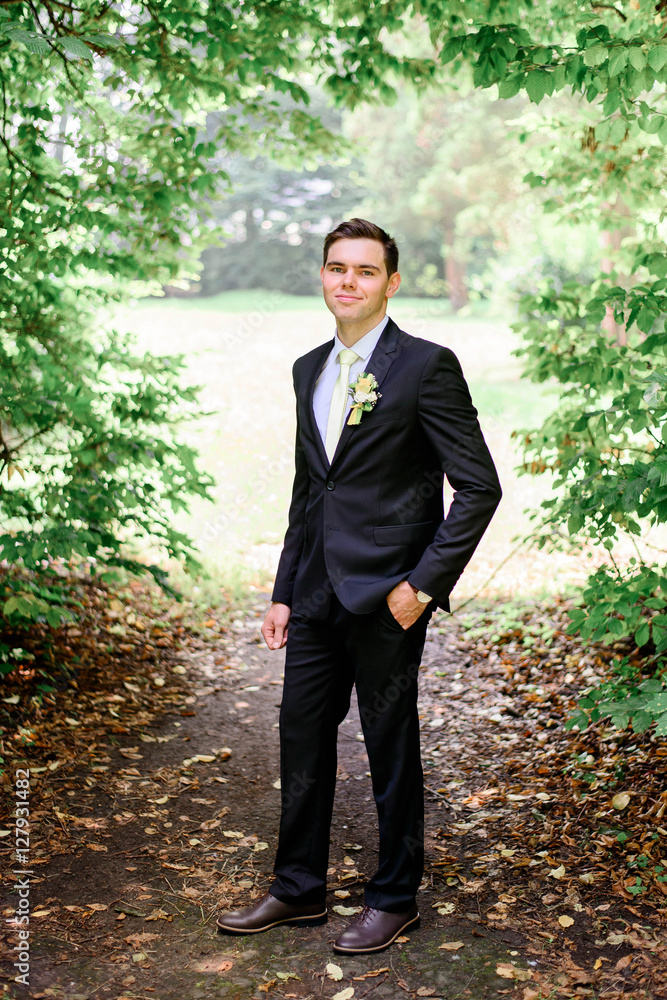 young handsome groom in a black suit standing alone outdoors young handsome groom in a black suit standing alone outdoors