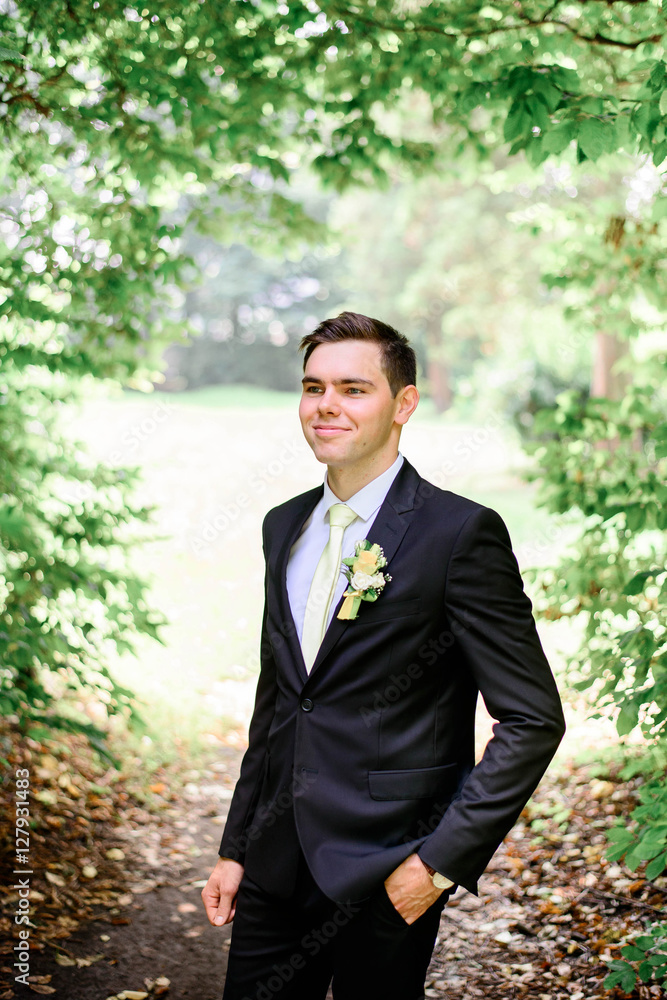 young handsome groom in a black suit standing alone outdoors young handsome groom in a black suit standing alone outdoors