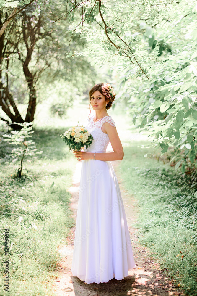 young beautiful bride in a white dress standing alone outdoors