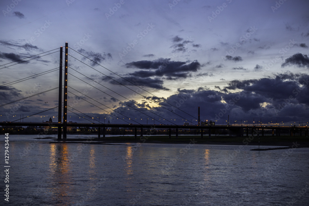 Fototapeta premium Beleuchtete Rheinkniebrücke in Düsseldorf an einem wolkenverhangenen Abend