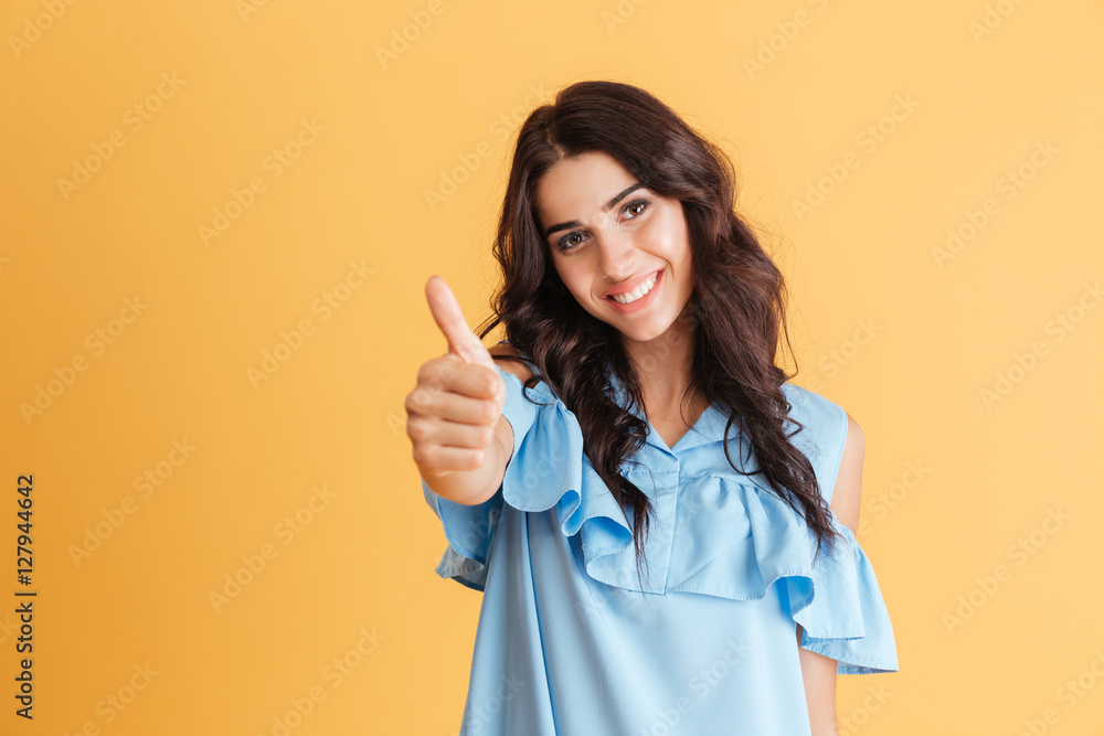 Smiling woman showing thumb up over orange background Smiling woman showing thumb up over orange background