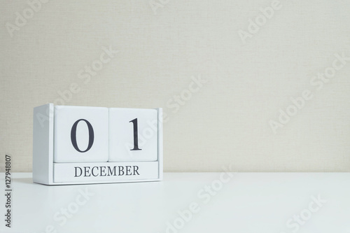 Closeup white wooden calendar with black 1 december word on blurred white wood desk and cream color wallpaper in room textured background with copy space , selective focus at the calendar