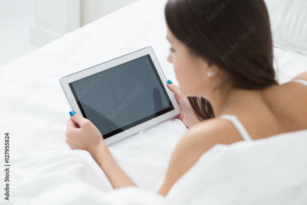 Woman lying in bed with her tablet PC and surfing internet