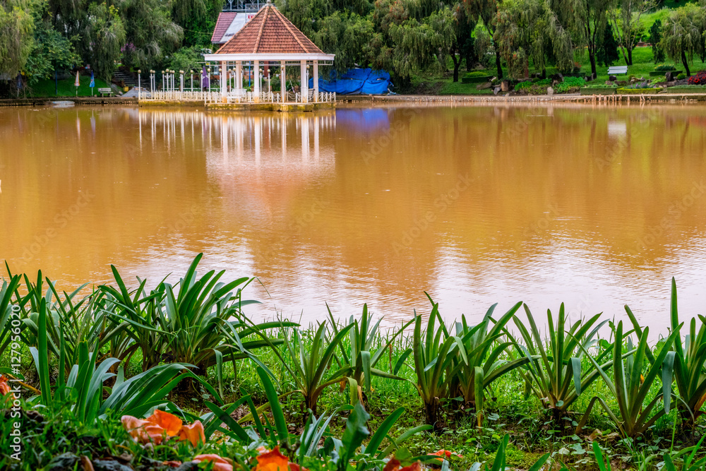 Bank of Pond with round pavilion on a water at a park of flowers at Vietnam