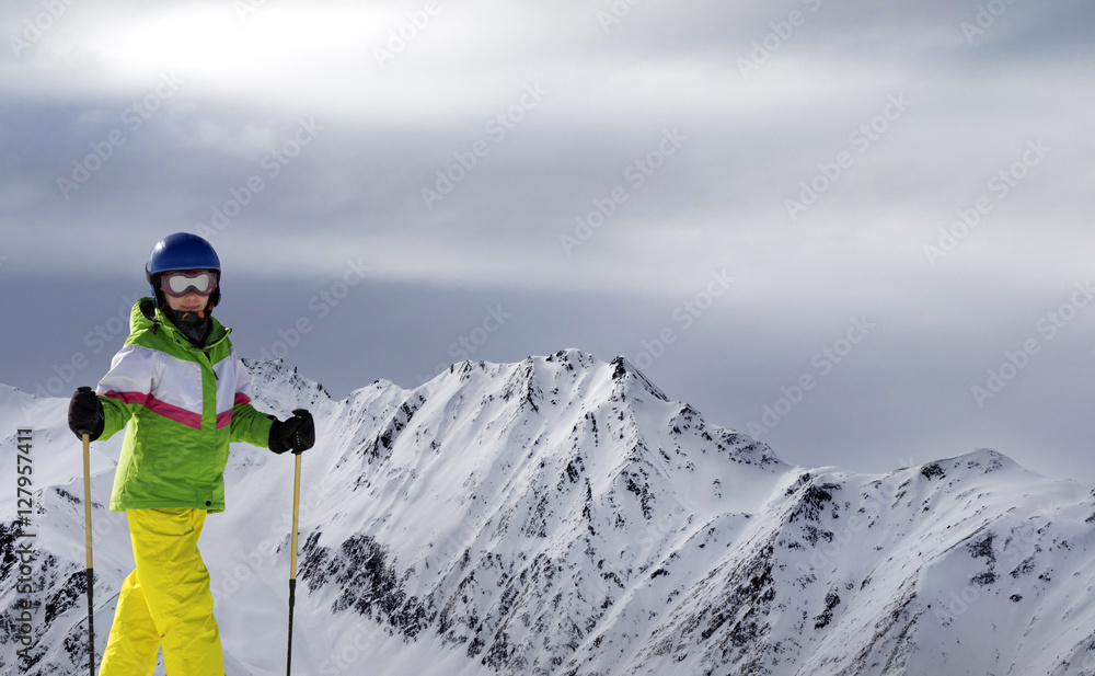 Young skier with ski poles in sunlight mountains and cloudy gray